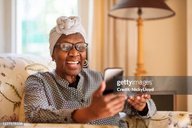 smiling senior woman video calling on her phone while sitting at home - africa phone black stock pictures, royalty-free photos & images