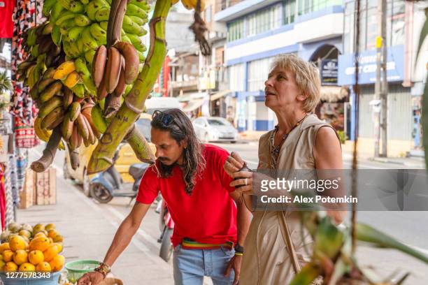 een sri lankaanse man helpt een europese toerist, 50 jaar oude actieve vrouw, om vers rijp fruit te plukken op een lokale straatmarkt in aluthgama, sri lanka - 50 54 years stockfoto's en -beelden