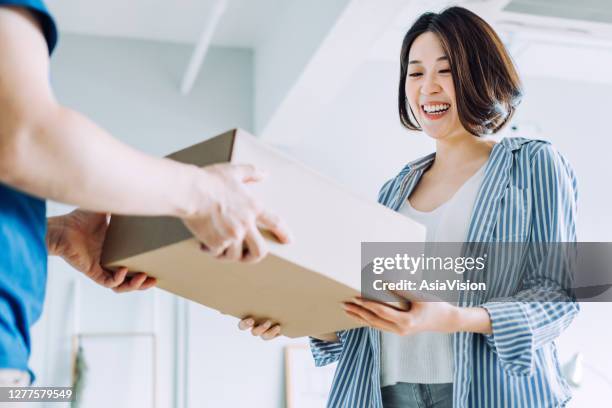 vista bassa dell'angolo di una giovane donna asiatica allegra che riceve un pacco da un fattorino a casa - consegna a domicilio foto e immagini stock