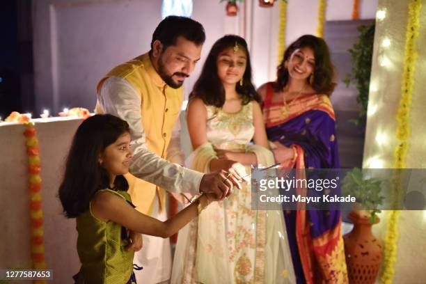 indian family in traditional wear lighting sparklers on the occasion of diwali - diwali family stock-fotos und bilder