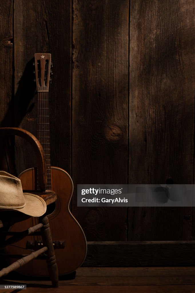 Guitar and cowboy hat with barnwood background with subdued lighting
