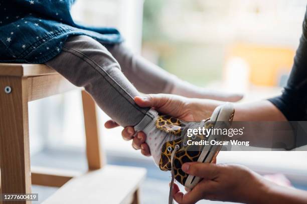 young mother helping daughter to put on shoes - vestirse fotografías e imágenes de stock