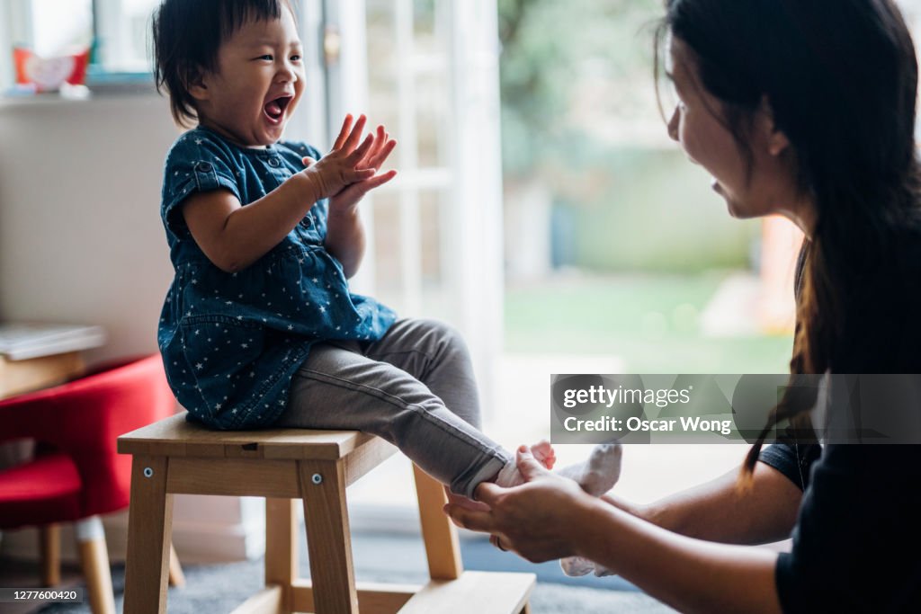 Young Mother Helping Daughter To Put On Socks