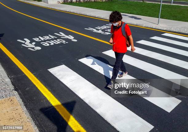 jongen in een rood t-shirt dat de weg met gezichtsmasker en celtelefoon kruist - cross stripes shirt stockfoto's en -beelden