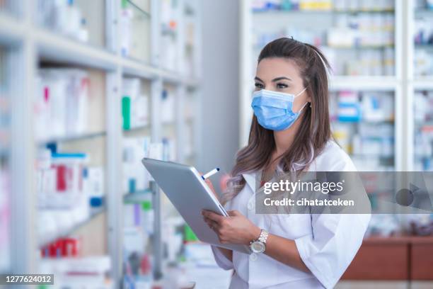la pharmacienne avec la tablette numérique utilisant un masque médical vérifie la prescription - fourniture médicale photos et images de collection