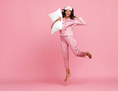 Excited woman in pajama jumping with pillow