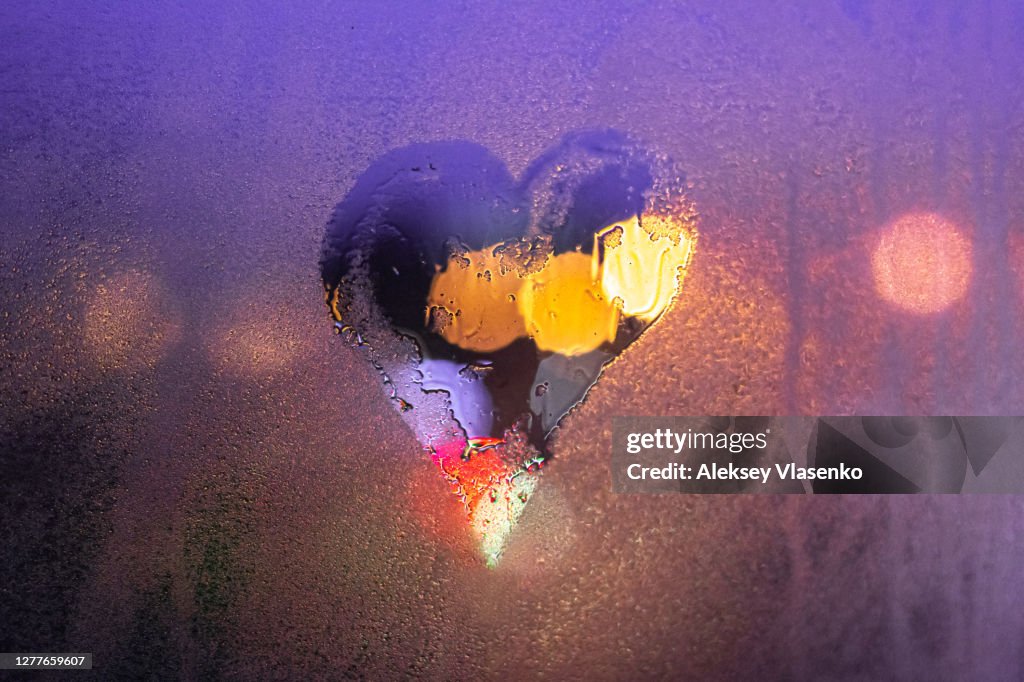 Close-up drawn heart on a foggy wet window