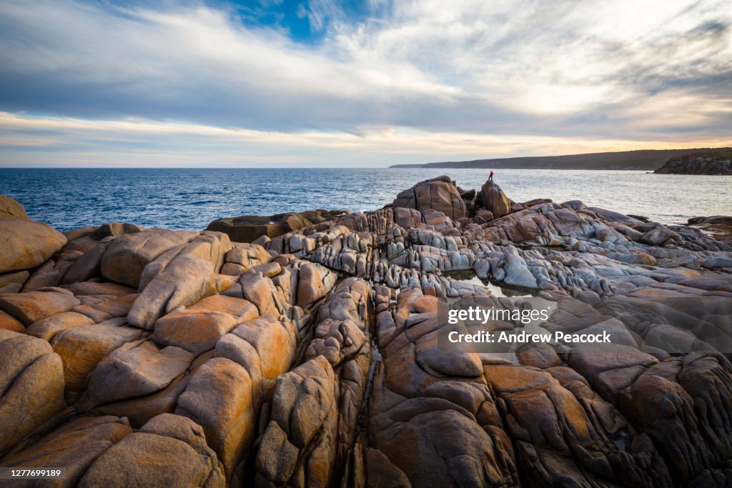 A woman standing on a large boulder in the distance at Windmill Bay