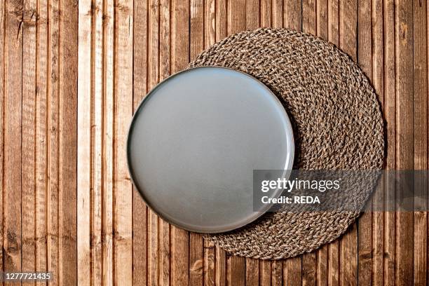 Empty ceramic plate on knitted straw round napkin over wooden plank background. Flat lay. Space.