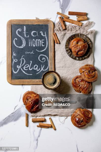 Traditional Swedish cinnamon sweet buns Kanelbulle on vintage tray. Cup of coffee on linen cloth. Chalkboard handwritten lettering Stay home and...