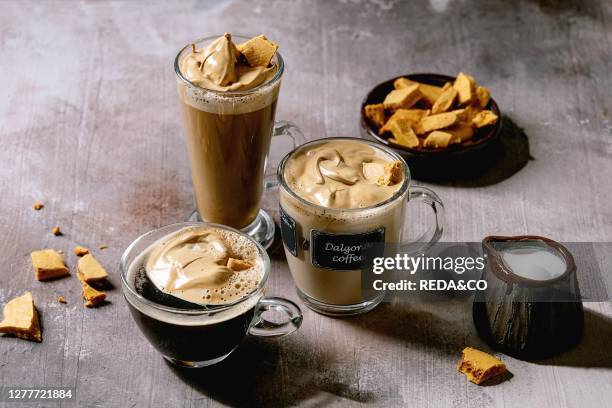 Dalgona frothy coffee trend korean drink latte espresso with coffee foam in three different glass cups. Decorated by dalgona cinder toffee candy....