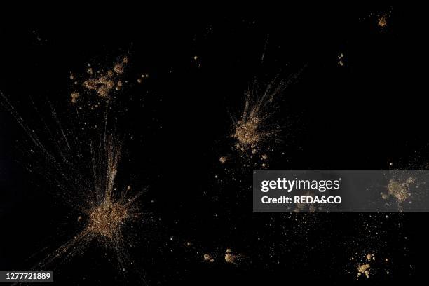 Golden powders splash and dust over black. Abstract design background.