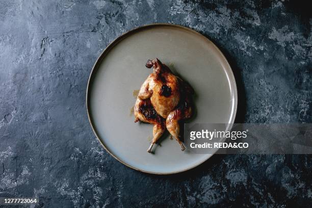 Roasted grilled butterfly quail on ceramic plate over black concrete background. Flat lay. Space.