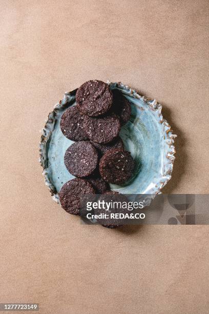 Homemade dark chocolate salted brownies cookies with salt flakes in blue ceramic plate over brown texture background. Flat lay, space.