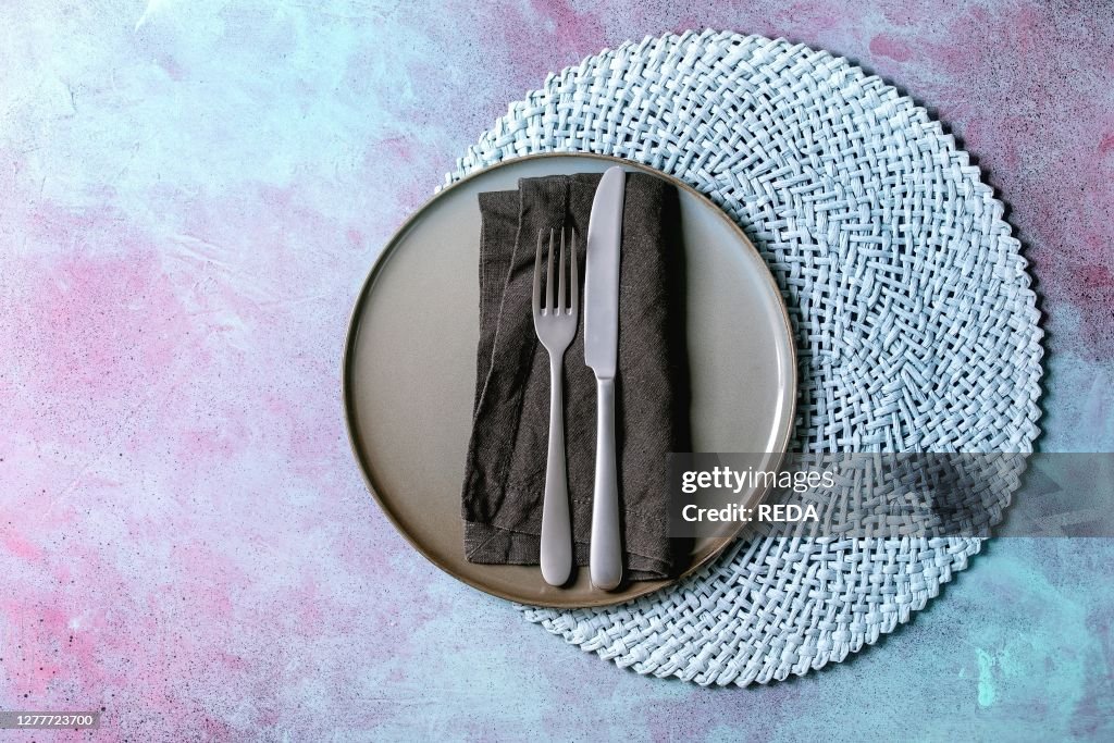 Empty ceramic plate with fork and knife on textile napkin on knitted round napkin over blue concrete background. Flat lay. space