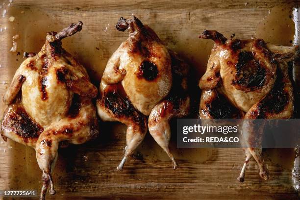 Three roasted grilled butterfly quails in glass baking tray over wooden background. Flat lay. Space.