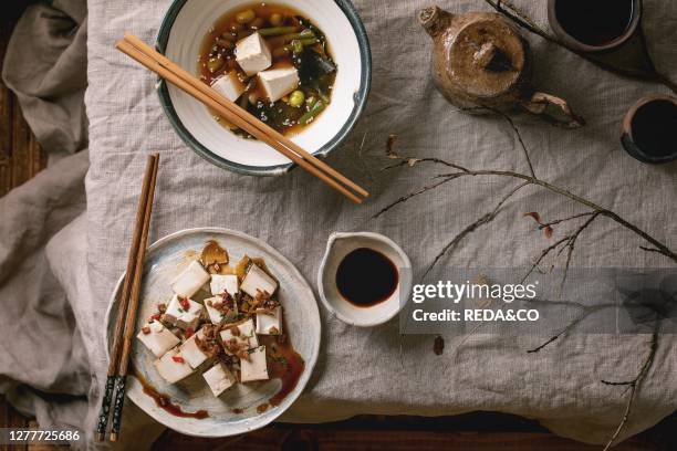 Japanese Miso broth soup with silk tofu cubes. Soy beans edamame. Green beans in traditional bowl with chopsticks. Ceramic teapot and cups on grey...