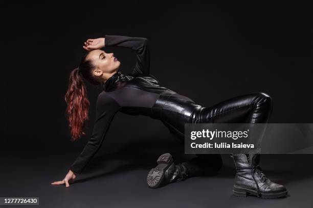 cool confident woman in black leather suit and boots in dark studio - leather pants photos et images de collection