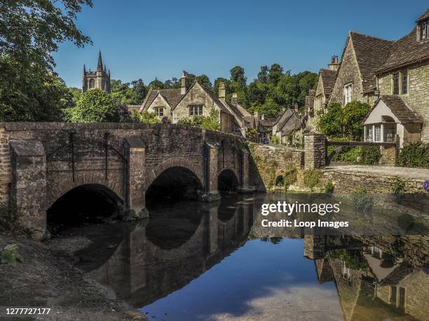 Stone bridge passing over a gentle stream leads the way into the village of Castle Combe in England.