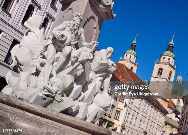 Slovenia, Ljubljana, Close up detail of the figures on the Robba Fountain with towers and dome of the Cathedral of St Nicholas in the background.