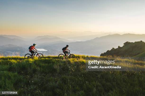 mountainbiker fahren auf grasbewachsenem bergrücken - fahrrad natur stock-fotos und bilder