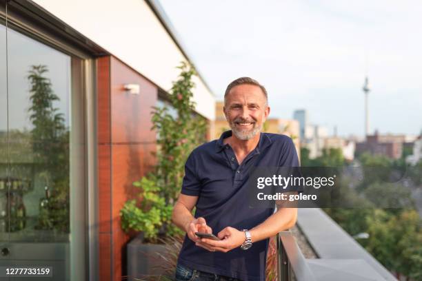 bärtiger mann im mittleren alter tippt auf handy auf balkon in berlin - nordeuropäischer abstammung stock-fotos und bilder