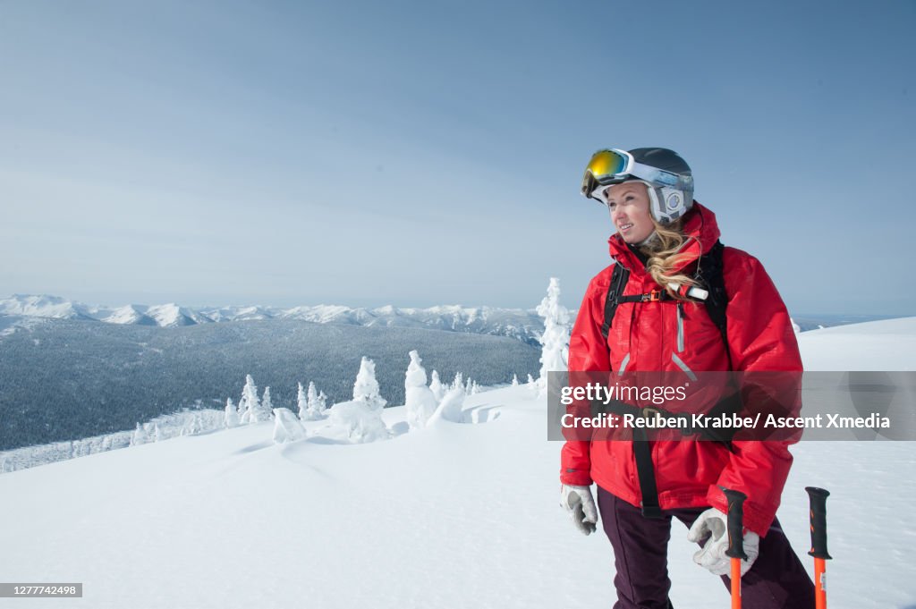 Young woman backcountry skier pauses on high mountain slope and looks out