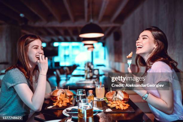 smiling female friends enjoying special burger dinner - fried chicken burger stock pictures, royalty-free photos & images