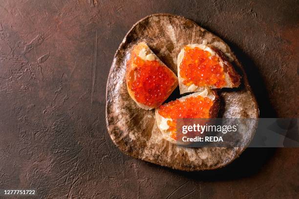 Red salmon caviar on wheat bread with butter on ceramic plate over dark brown texture background. Flat lay. Space.