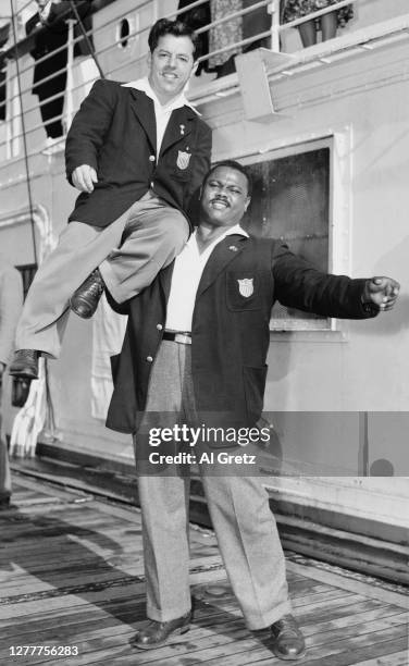 American heavyweight weightlifter John Davis lifts bantamweight weightlifter Joseph DePietro on the deck of the 'SS Washington', as they return to...