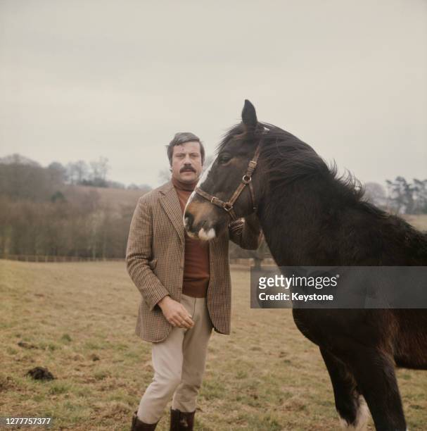 English actor Oliver Reed with a horse in the countryside near his home, UK, circa 1973.