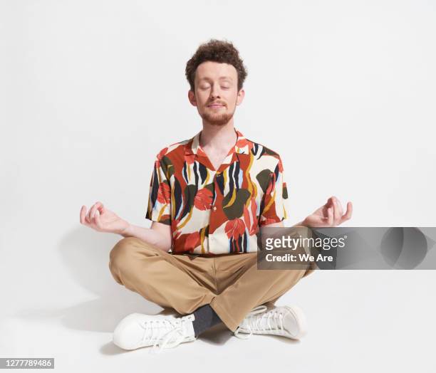 young man sitting in mediation pose - low key stock-fotos und bilder