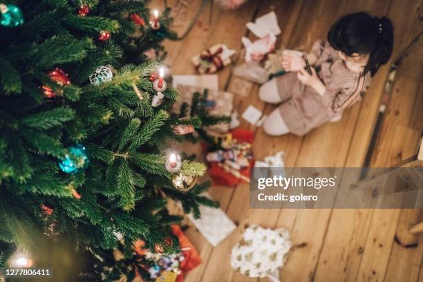 girl unwrapping christmas gifts under the christmas tree - unwrapped stock pictures, royalty-free photos & images