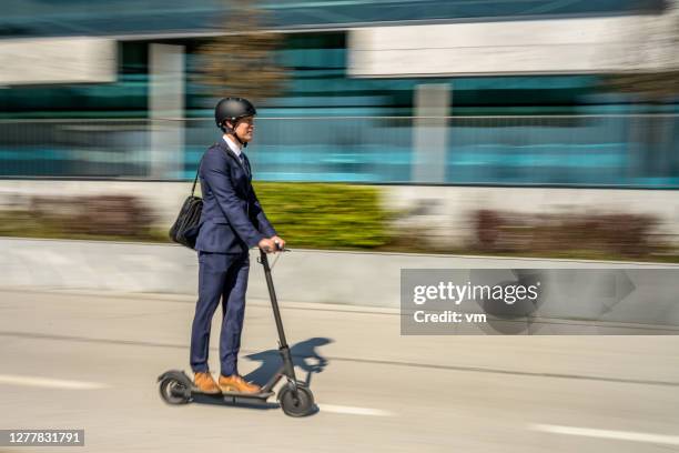 businessman riding an electric push scooter through the city - push scooter stock pictures, royalty-free photos & images