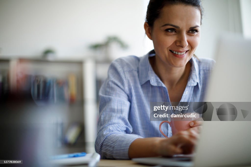 Lächelnde reife Frau mit Laptop für die Arbeit zu Hause