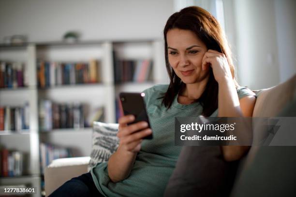 donna matura sorridente che usa il cellulare a casa - friends chatting mature foto e immagini stock