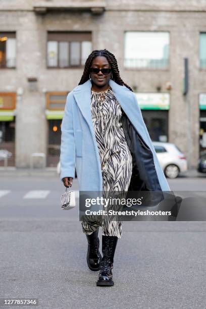 Influencer Lois Opoku, wearing a blue coat by Kaos, a safari dress by Kaos, boots by Jeffrey Campbell, a black and white safari bag by Weat and...