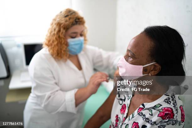 verpleegster die vaccin op de wapen van de patiënt toepast gebruikend gezichtsmasker - allergy doctor stockfoto's en -beelden