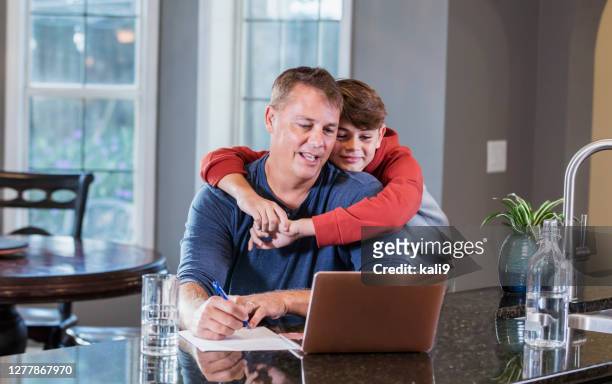 man working from home on computer, son giving him hug - boy looking over shoulder stock pictures, royalty-free photos & images
