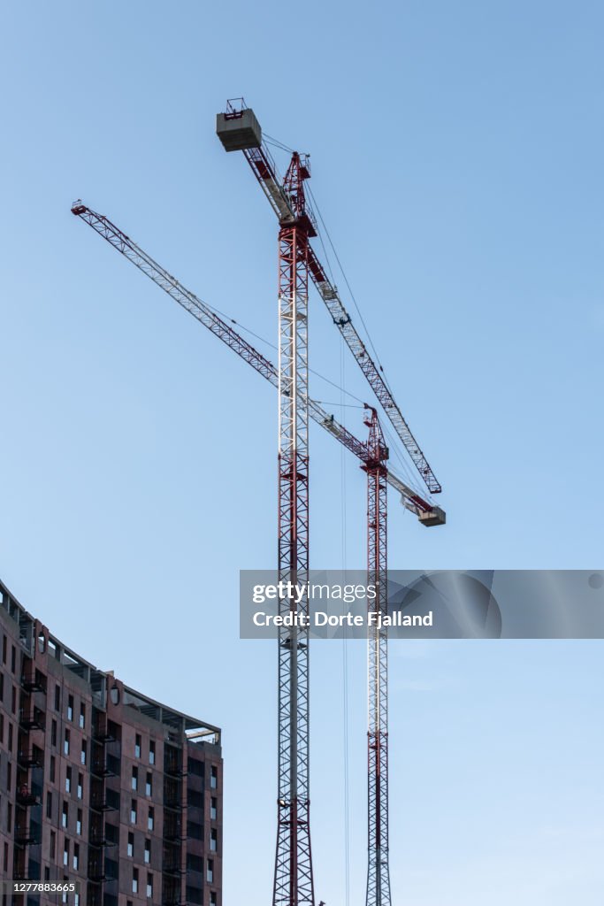 Two tall cranes next to a building and a clear blue sky