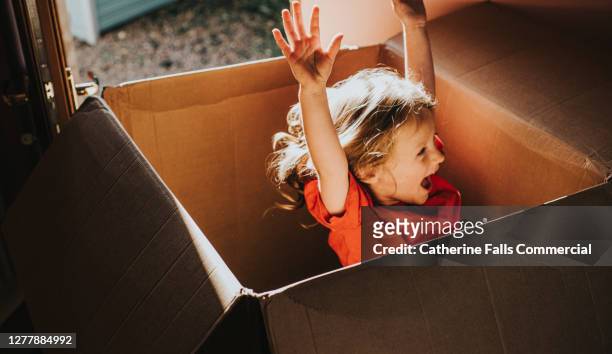 excited little girl jumping inside a huge cardboard box - aufregung stock-fotos und bilder