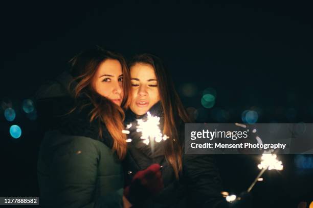 cheerful two young women holding a sparkler in hand at night christmas new year - two year anniversary party stock pictures, royalty-free photos & images