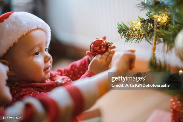 beautiful portrait of a baby girl that is wearing christmas hat and playing with a christmas decoration - xmas tree snow lights silly stock pictures, royalty-free photos & images