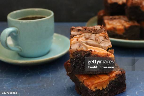 close-up image of homemade chocolate salted caramel brownie squares piled on green plate and on slate, green coffee cup and saucer, focus on foreground - salted brownie stock pictures, royalty-free photos & images