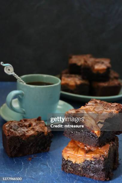 close-up image of homemade chocolate salted caramel brownie squares piled on green plate and on slate, metal spoon, green coffee cup and saucer, focus on foreground - caramelized stock pictures, royalty-free photos & images