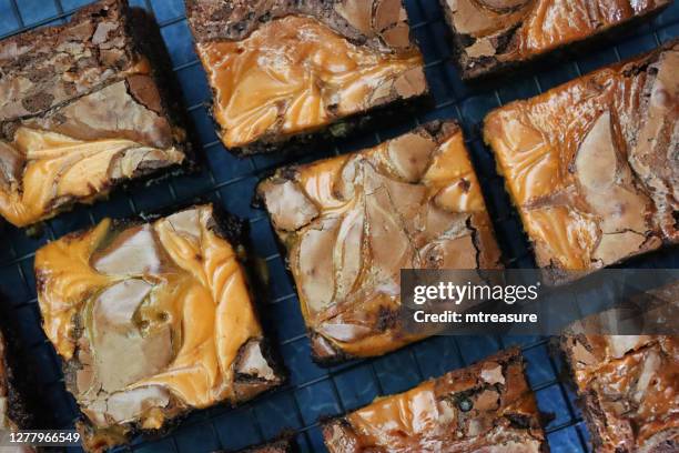 close-up image of homemade chocolate salted caramel brownie squares on metal cooling rack, grey slate background, elevated view - salted brownie stock pictures, royalty-free photos & images