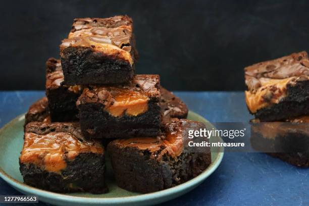 close-up image of homemade chocolate salted caramel brownie squares piled on green plate and on slate table top, focus on foreground - caramel stock pictures, royalty-free photos & images