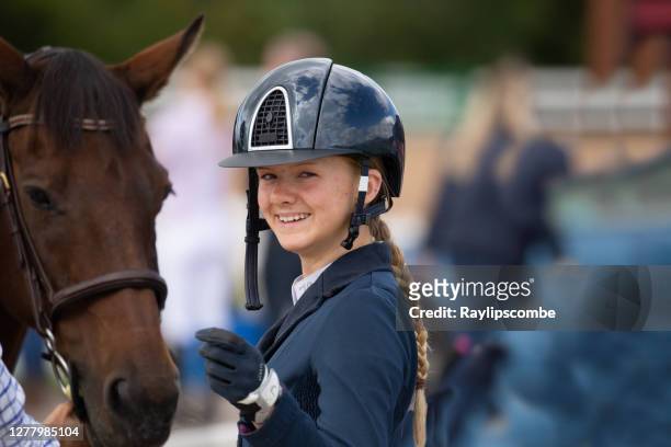 gelukkige, glimlachende jonge ruiter in een beschermende berijdende helm die door haar paard wordt bevonden. - happy jumping stockfoto's en -beelden