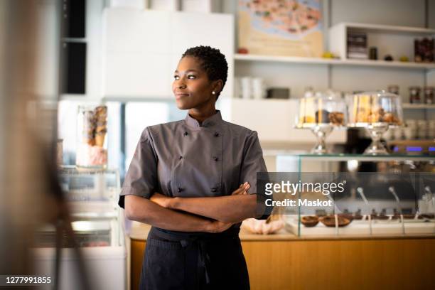 smiling chef with arms crossed looking away in chocolate factory - small business stock pictures, royalty-free photos & images
