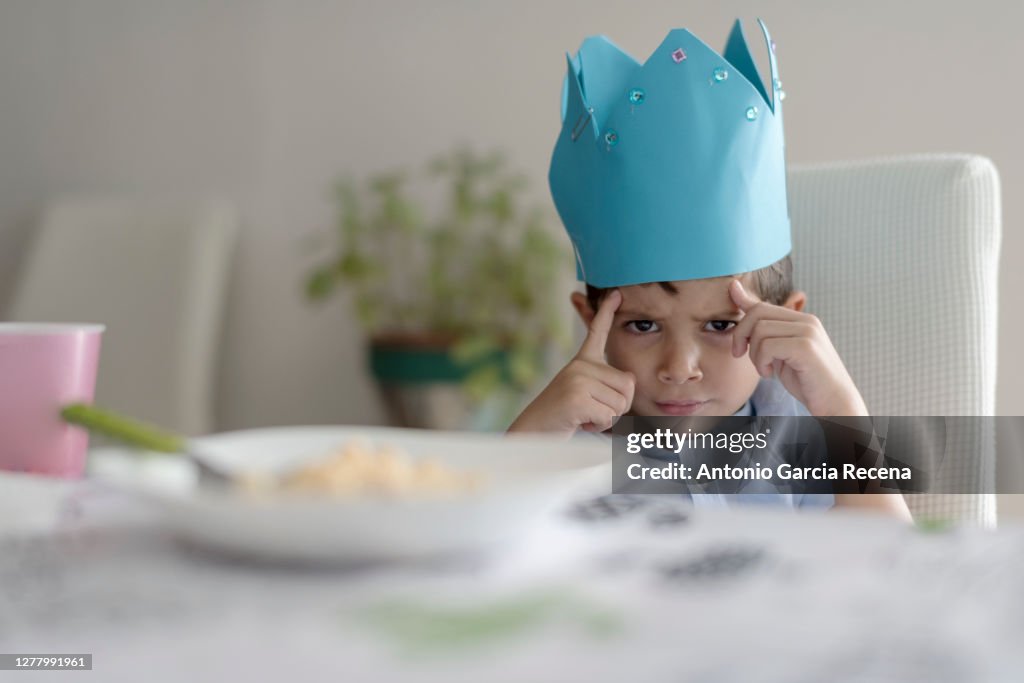 Child with foam crown eats macaroons at home. king of home.